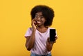 Pretty african american bushy woman showing smartphone with empty screen, advertising new app on yellow background