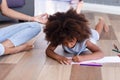 Pretty African American girl drawing pencils while mother meditating