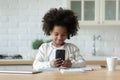 Pretty African American little girl using phone, distracted from studying