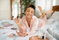 Pretty african american woman applying nail polish, making manicure while lying on bed at home Royalty Free Stock Photo