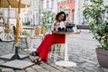 Pretty African American woman, sitting in outdoor city cafe at the table, holding paper cup of coffee and croissant Royalty Free Stock Photo