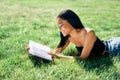 Pretty afro american woman reading book lying in grass in park Royalty Free Stock Photo