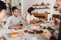 Pretty afro american woman sitting at the table thoughtfully talking while man near happily cutting bread. Group of Royalty Free Stock Photo