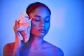 Pretty afro woman with closed eyes pressed seashell to her ear enjoy and dreams in neon light Royalty Free Stock Photo