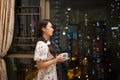 Pretty Asia university female students driink tea or wine near window with blurred bokeh colorful City light background Royalty Free Stock Photo