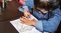 Pretty asian child right handed while doing a coloring activity with crayon and coloring book