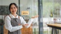 A pretty Asian female cafe staff or small business owner stands with a friendly welcome gesture Royalty Free Stock Photo