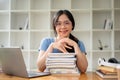 A pretty Asian female college student in glasses sits at her study table with a stack of books Royalty Free Stock Photo