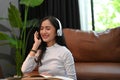 Pretty Asian female listening to music with her headphones while relaxing in living room Royalty Free Stock Photo
