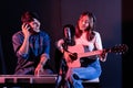 Pretty Asian female singer playing acoustic guitar with male playing electric keyboard. Recording songs by using a studio Royalty Free Stock Photo