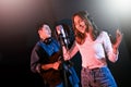 Pretty Asian female singer recording songs by using a studio microphone and pop shield on mic with male playing guitar. Royalty Free Stock Photo