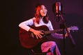 Pretty Asian female singer recording songs by using a studio microphone and pop shield on mic while playing guitar. Royalty Free Stock Photo