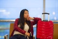 Pretty Asian Korean tourist woman sitting at airport departure gate with suitcase hand luggage holding passport and boarding pass Royalty Free Stock Photo