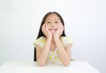 Pretty Asian little child girl resting chin on hands on table over white background