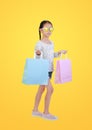Pretty Asian little child girl wearing sunglasses holding shopping bags on yellow  background with clipping path. Full Royalty Free Stock Photo