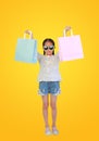 Pretty Asian little child girl wearing sunglasses holding shopping bags on yellow isolated background with clipping path. Full Royalty Free Stock Photo