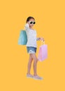 Pretty Asian little child girl wearing sunglasses holding shopping bags on yellow isolated background with clipping path. Full Royalty Free Stock Photo
