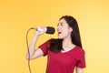 Pretty Asian woman in casual wear holding microphone and singing on yellow background Royalty Free Stock Photo