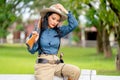 Pretty Asian woman with cowboy style hold rifle gun on her shoulder also touch her hat and sit on fence in farm with day light Royalty Free Stock Photo