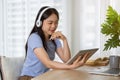 A pretty Asian woman listening to music through her headphones while using her tablet at a table Royalty Free Stock Photo