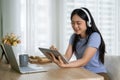 A pretty Asian woman listening to music through her headphones while using her tablet at a table Royalty Free Stock Photo