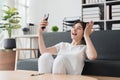 Pretty Asian woman sit on sofa at home enjoy with video call meeting with friend. Woman making content by smartphone at Royalty Free Stock Photo