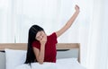 Pretty Asian woman sitting on a clean white bed, She covered her mouth and yawning After she woke up