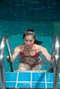 Pretty Asian woman wearing red bikini swim and standing at stair at swimming pool. Royalty Free Stock Photo