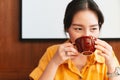 A pretty Asian woman wearing a yellow shirt is drinking coffee in the cafe with happy eyes. Enjoyment female lifestyle. Royalty Free Stock Photo