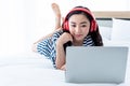 Pretty Asian woman, 23 years old, Wears red headphones She smiles happily while using a notebook computer On her white bed Royalty Free Stock Photo