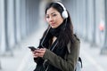 Pretty asian young woman listening to music and looking at camera in the street. Royalty Free Stock Photo