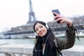 Pretty asian young woman taking a selfie in front of Eiffel tower in Paris while listening to music. Royalty Free Stock Photo