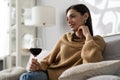 Pretty, attractive, stylish young woman sitting on couch having raised glass with red wine, examine, taste beverage