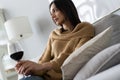 Pretty, attractive, stylish young woman sitting on couch having raised glass with red wine, examine, taste beverage