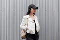 Pretty attractive woman in a fashionable black baseball cap in a stylish white leather jacket in jeans Royalty Free Stock Photo