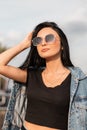 Pretty attractive young hipster woman in black top in a denim blue jacket in stylish black sunglasses relaxes Royalty Free Stock Photo