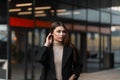 Pretty attractive young woman fashion model straightens hair outdoors in a spring day. Beautiful cute girl in a stylish black coat Royalty Free Stock Photo