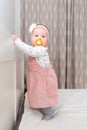 A pretty baby girl in a dress, with a pacifier in her mouth and with a headband on her head, stands near the crib. The concept of Royalty Free Stock Photo