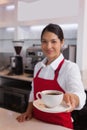 Pretty barista offering cup of coffee smiling at camera Royalty Free Stock Photo