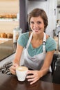 Pretty barista offering cup of coffee smiling at camera Royalty Free Stock Photo