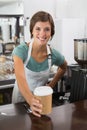 Pretty barista smiling at camera holding disposable cup Royalty Free Stock Photo
