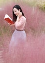 Pretty beautiful cute Asian Chinese woman girl reading book in a flower field outdoor in summer autumn fall park grass lawn garden Royalty Free Stock Photo
