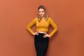 Pretty beautiful young blonde girl with plump lips and large breasts, stands with her hands on hips, in yellow blouse and black Royalty Free Stock Photo