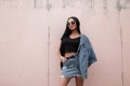 Pretty beautiful young hipster woman in a stylish denim jacket in a trendy black top in a vintage jeans skirt in sunglasses Royalty Free Stock Photo