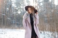 Pretty beautiful young woman in a black knitted dress in an elegant black hat in a stylish pink coat posing outdoors Royalty Free Stock Photo