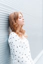 Pretty beautiful young woman with blond hair in a stylish white pullover resting near the modern metal wall in the city. Royalty Free Stock Photo