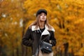 Pretty beautiful young woman in a brown stylish jacket in an elegant hat with a visor with a leather trendy bag posing in the park Royalty Free Stock Photo