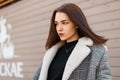 Pretty beautiful young woman model in an elegant spring gray plaid coat in a black trendy T-shirt stands