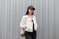 Pretty beautiful young woman with a stylish gold backpack in a fashionable white leather jacket in black jeans Royalty Free Stock Photo
