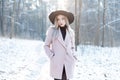 Pretty beautiful young woman in stylish warm glamorous clothes is walking in an elegant hat in a snowy forest Royalty Free Stock Photo